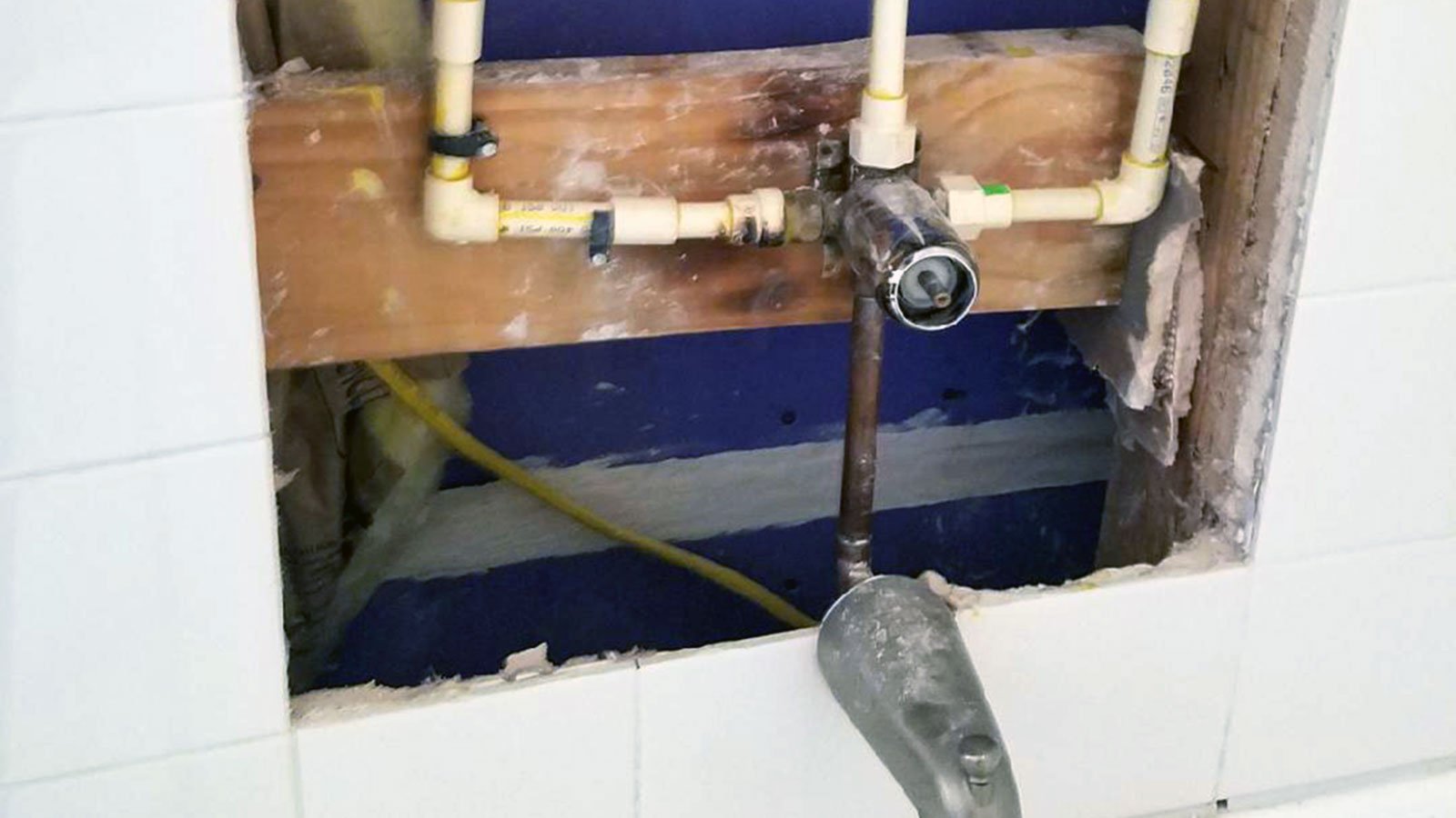 Exposed bathtub faucet and plumbing in a university apartment after tiles were removed to access burst pipes.