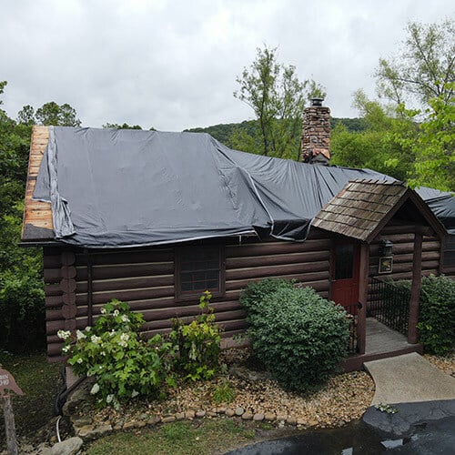 Log cabin at remote resort after fire damage with temporary tarping for roof.