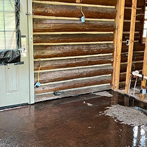 Inside view of log cabin facing fire damages and flooding near electrical wiring.